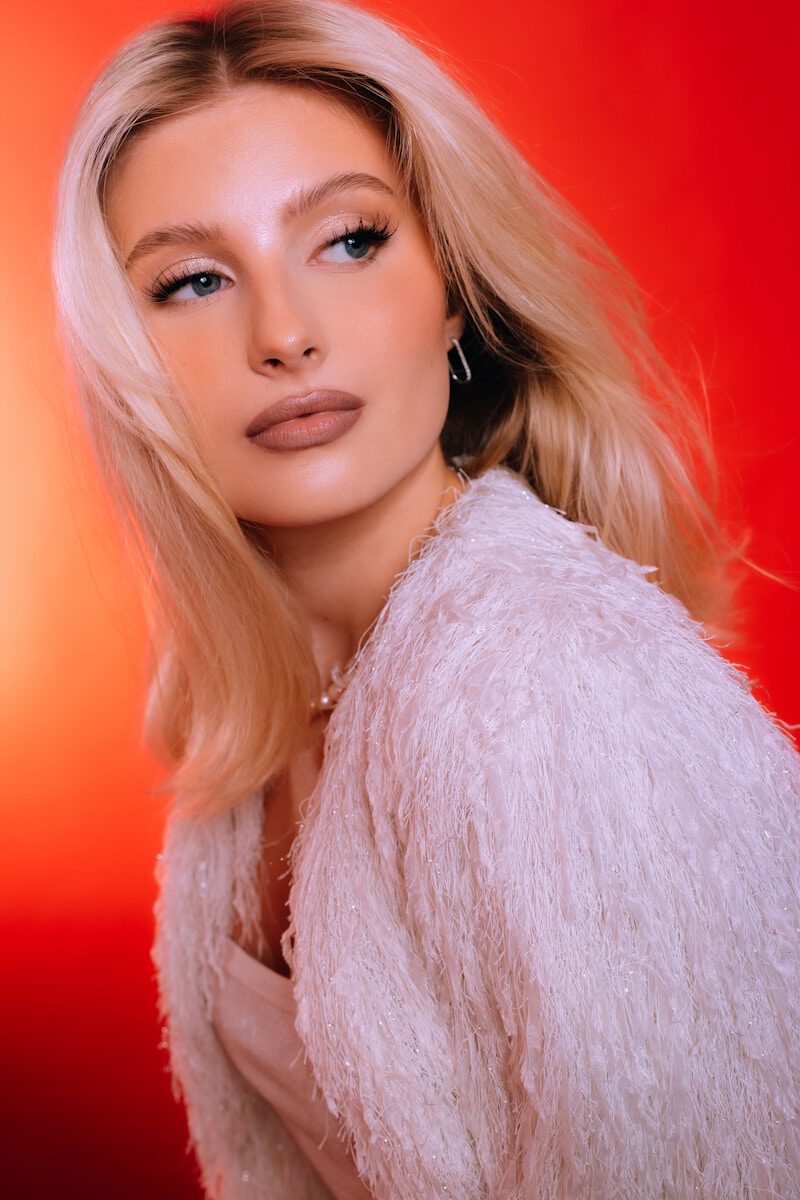 Blonde woman in white fluffy jacket against a red background.